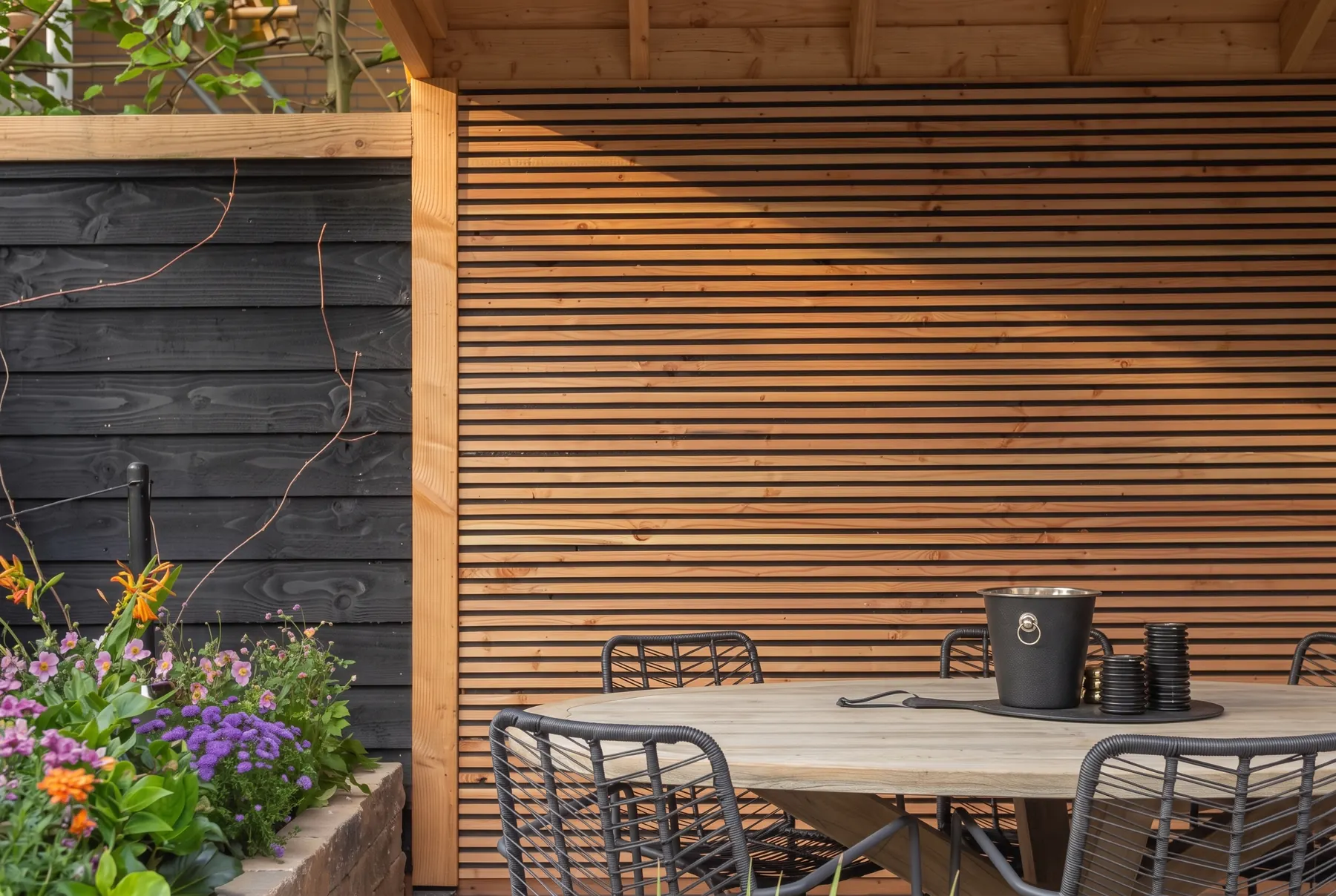 Lamellenwand in douglas onder een houten overkapping, met tuintafel in het avondlicht